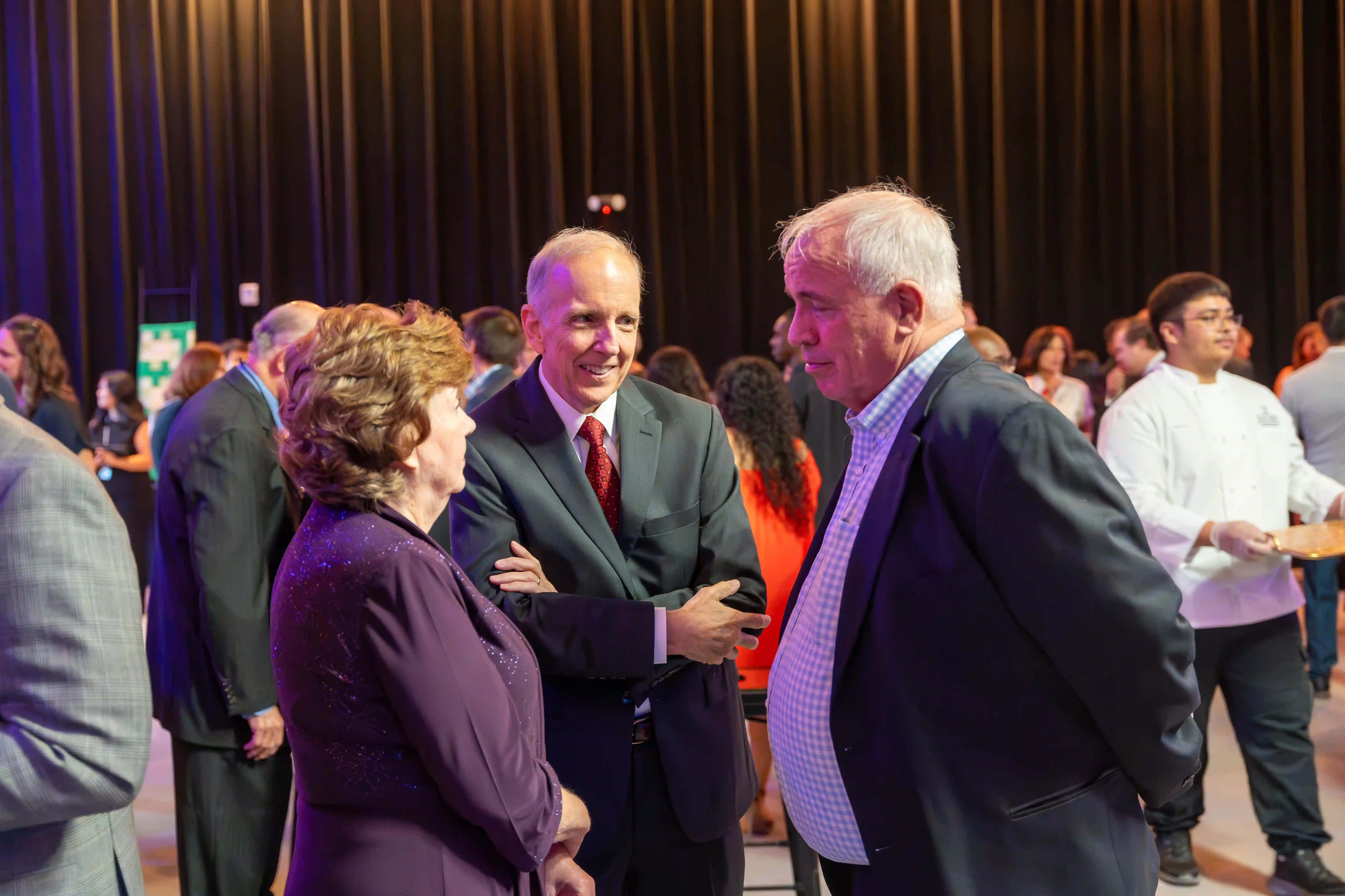 Jeanne Norskov, Rick Norskov, and Rahn Shaw talking together amongst the other guests