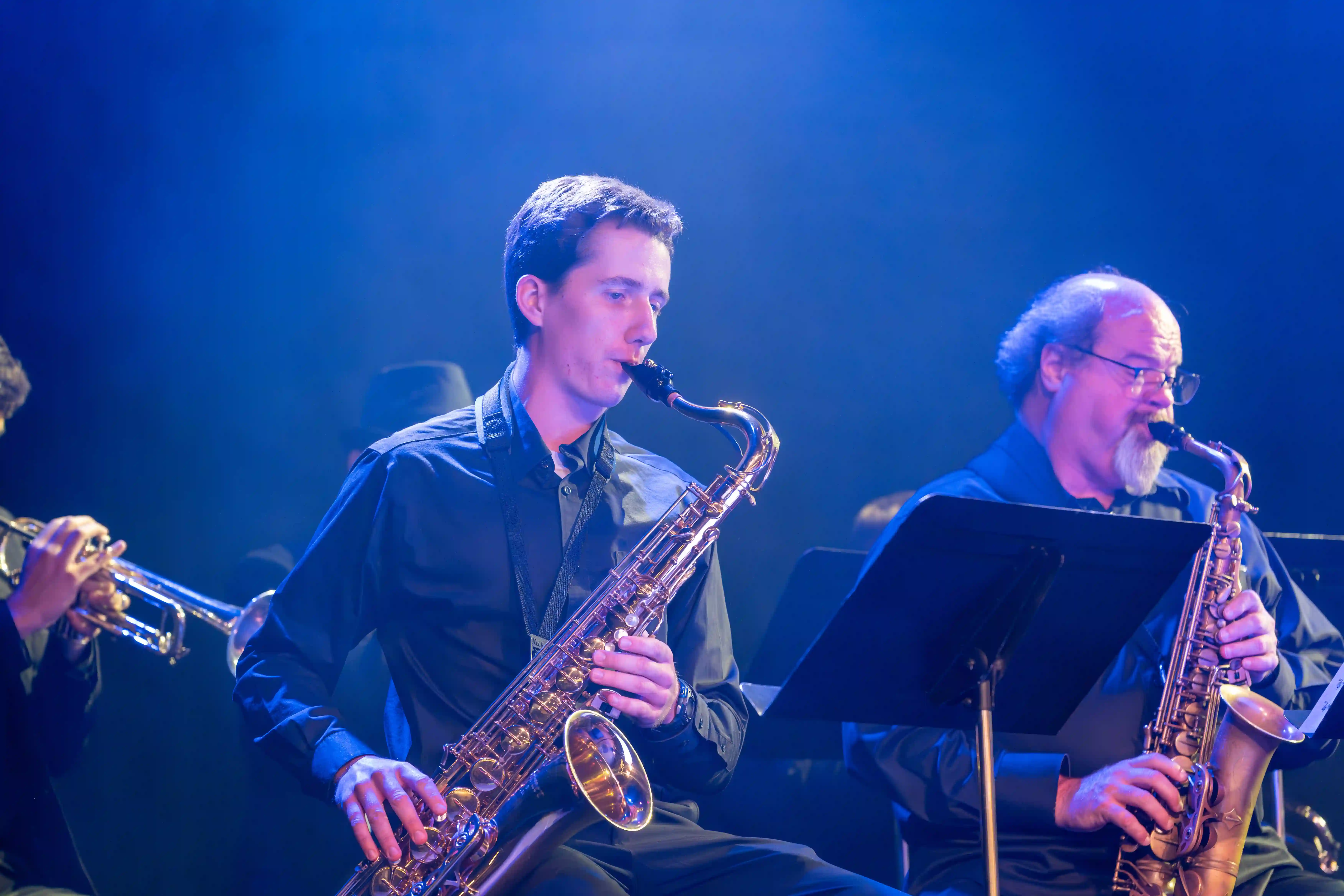 Two saxophone players performing on stage under a blue light