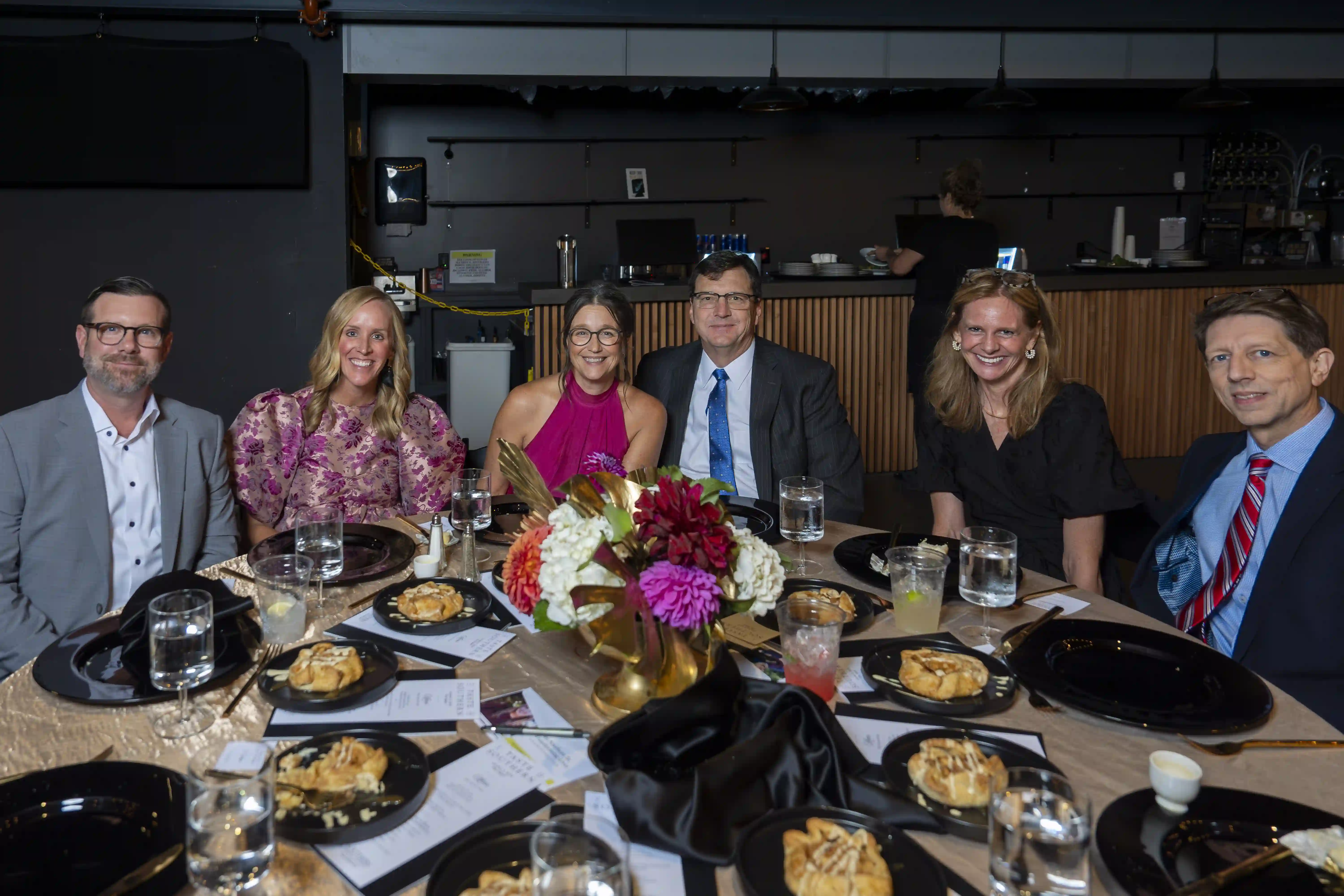 Jon Hughes, Kera Hughes, Greg Willett '89, Terri Willett, Austin Pedigo, Stephany Pedigo sit at a round table posing for the picture during the dinner portion of the evening.