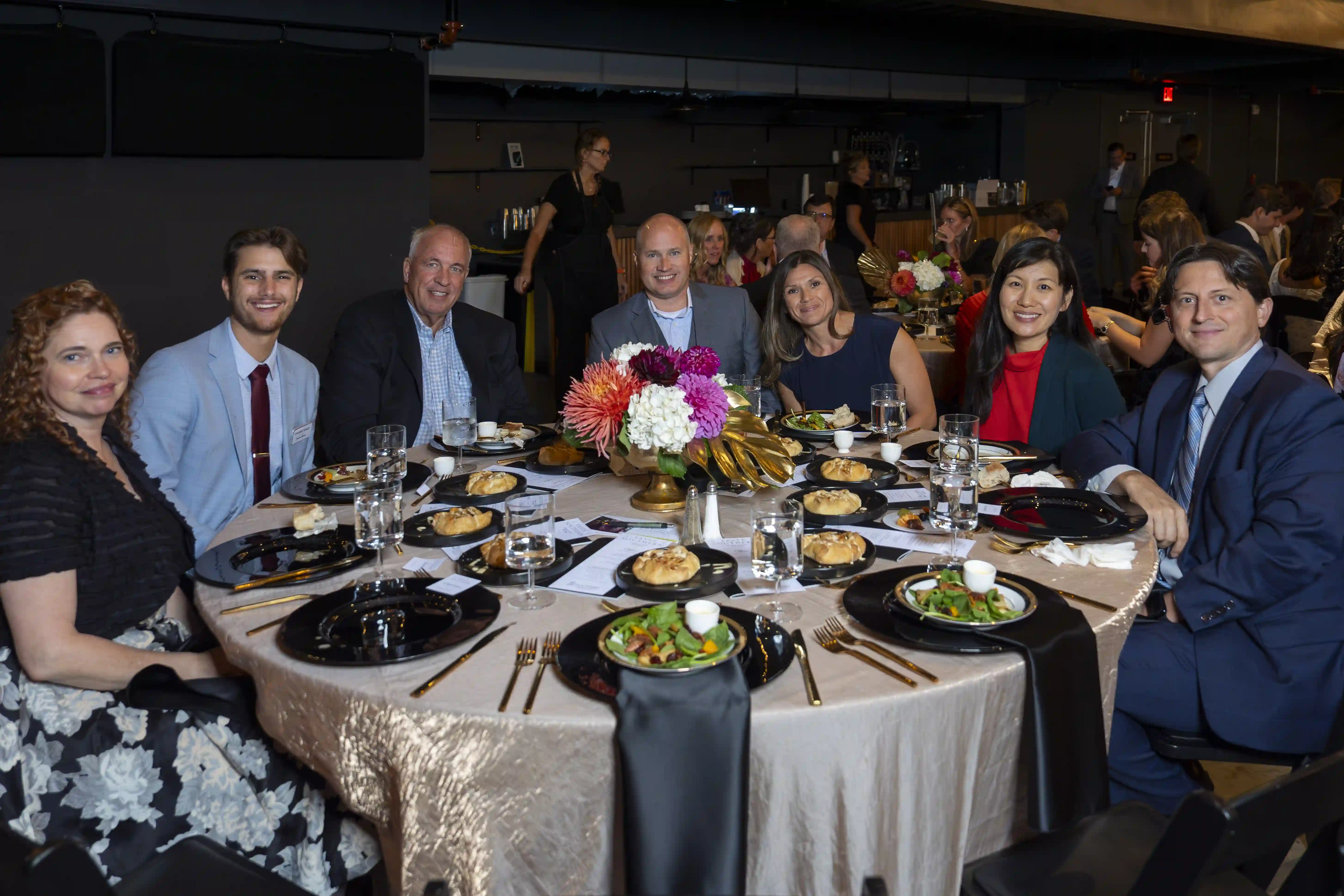 LeAnn Gariepy, Preston Waters, Rahn Shaw, Gary Rustad, Dee Rustad, Jane Clark, Chester Clark sit at a round table posing for the picture during the dinner portion of the evening.