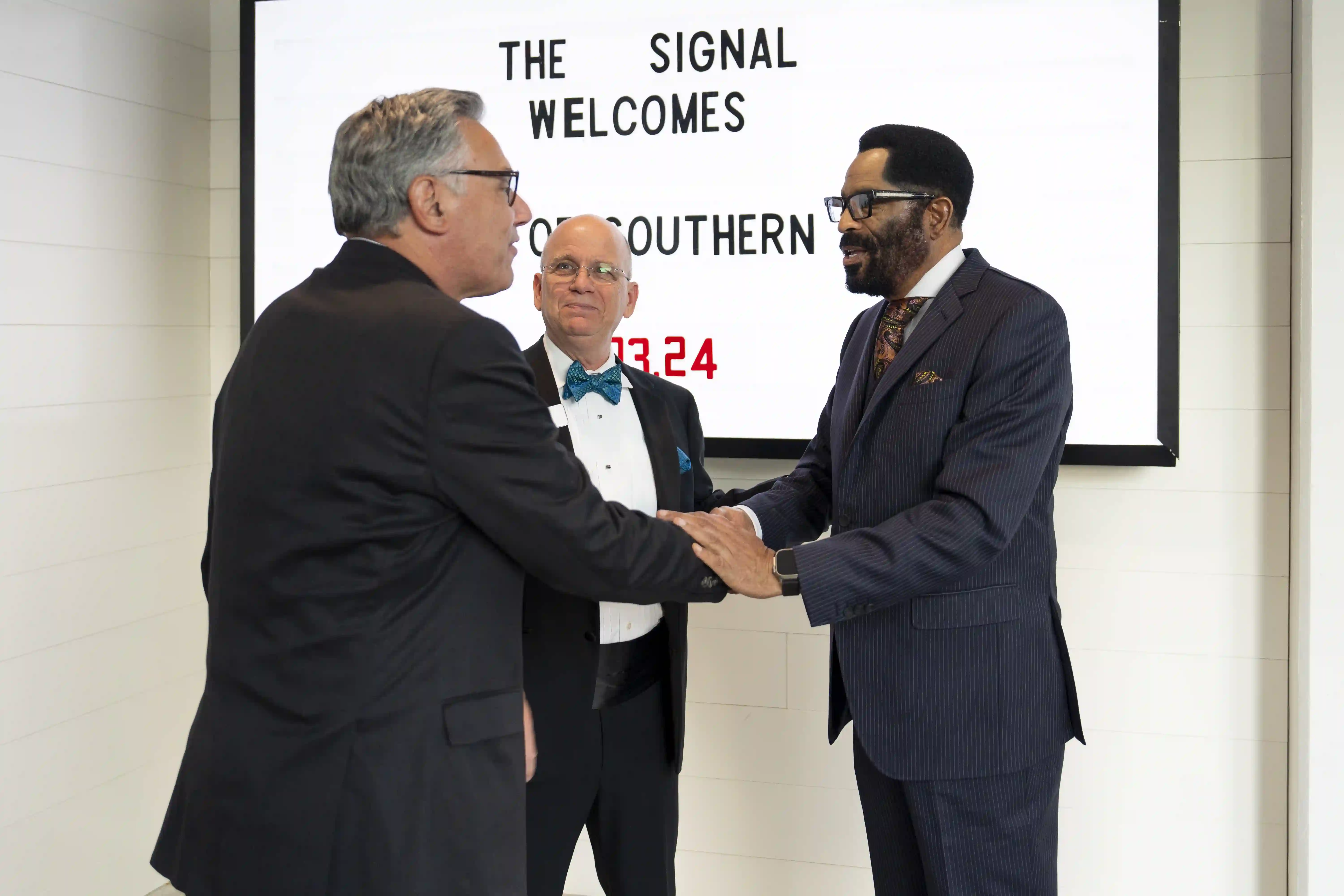 Greg Vital and Ron Smith shaking hands with each other in front of Ken Shaw