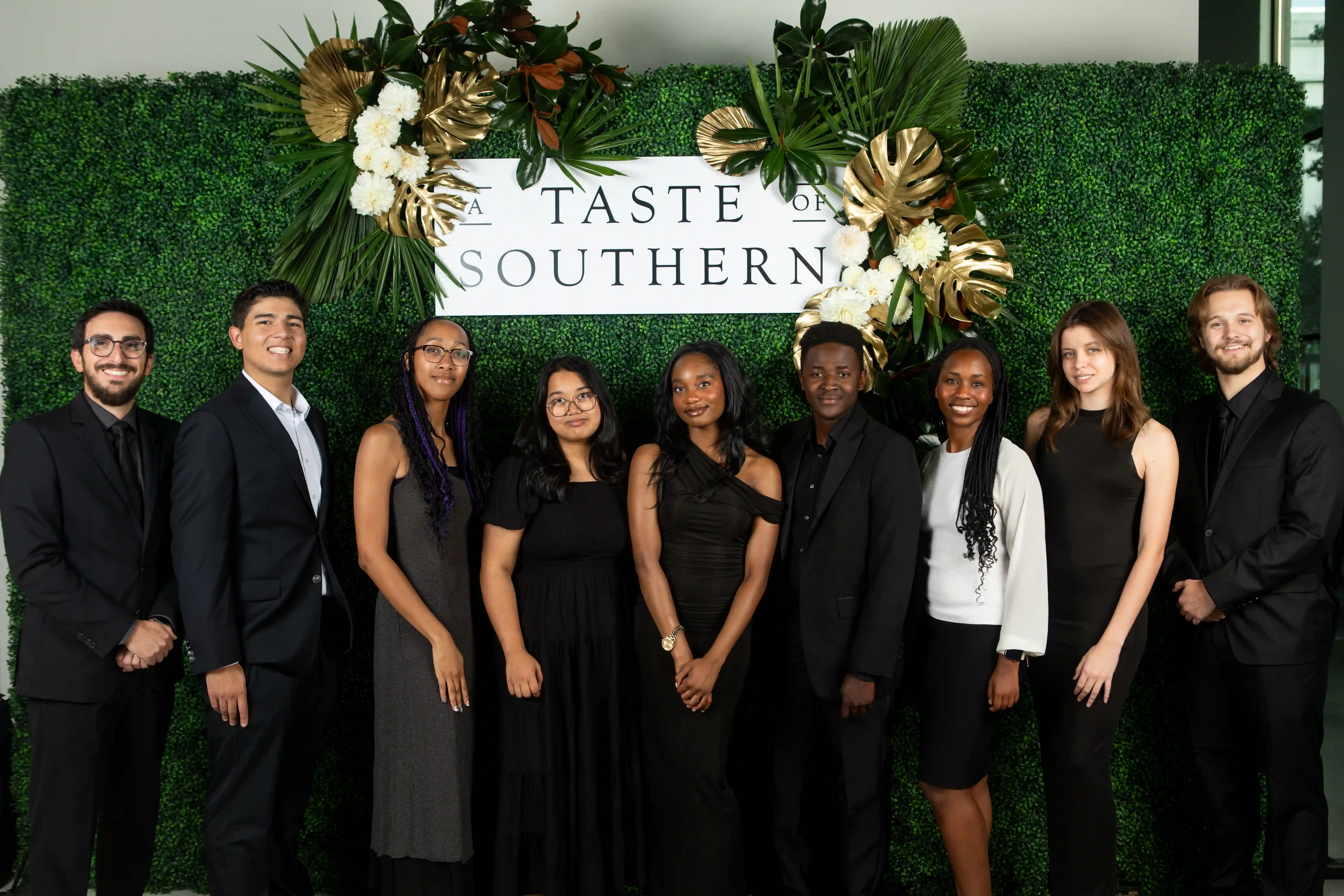 A group of School of Journalism and Communication students and faculty posing in front of a green backdrop