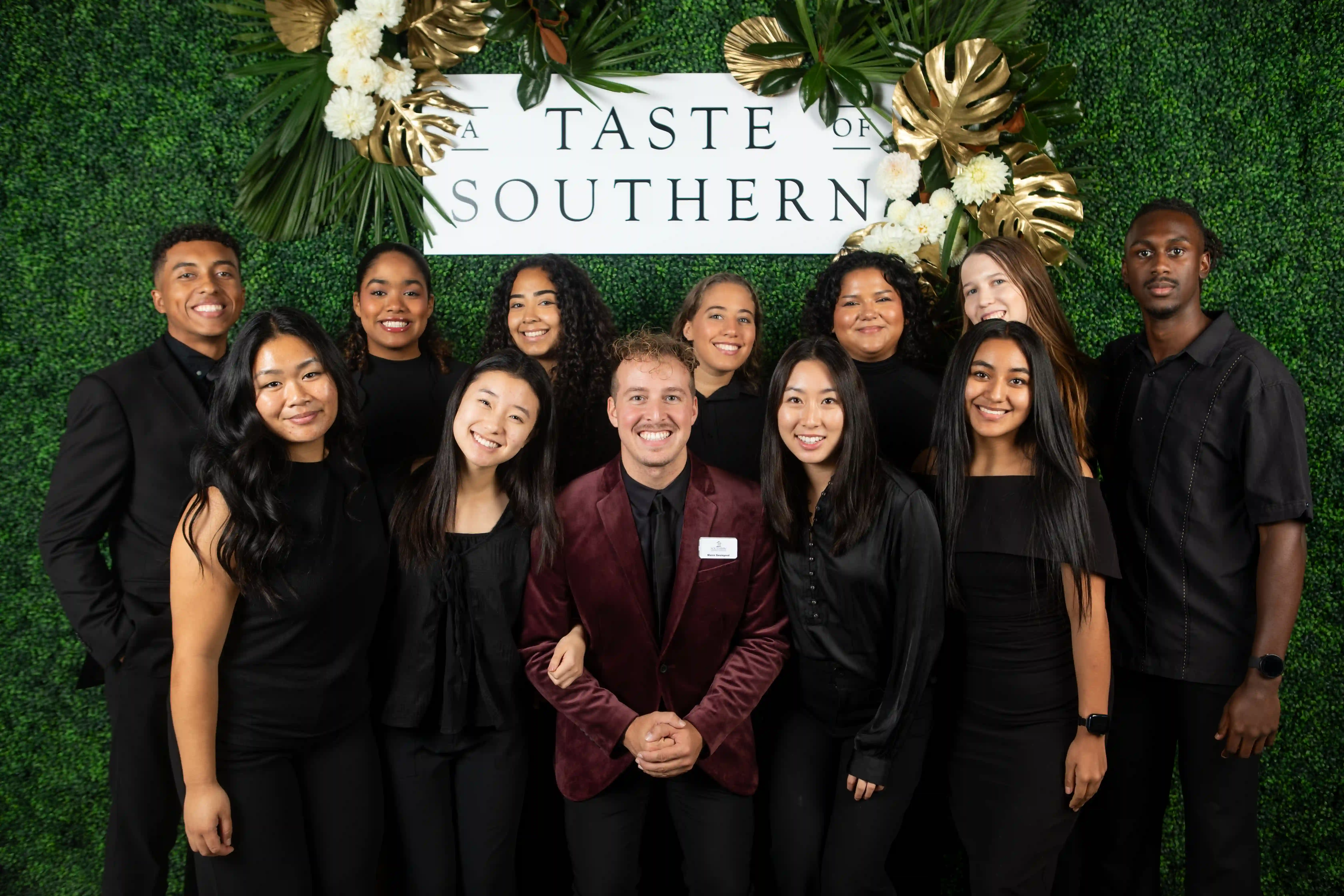 A group of students and staff dressed in black, posing in front of a green backdrop