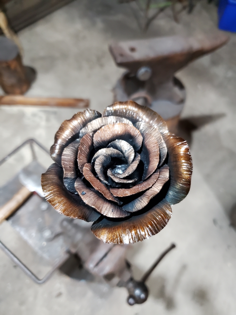 Steel rose in the foreground and blacksmithing tools blurred in the background.