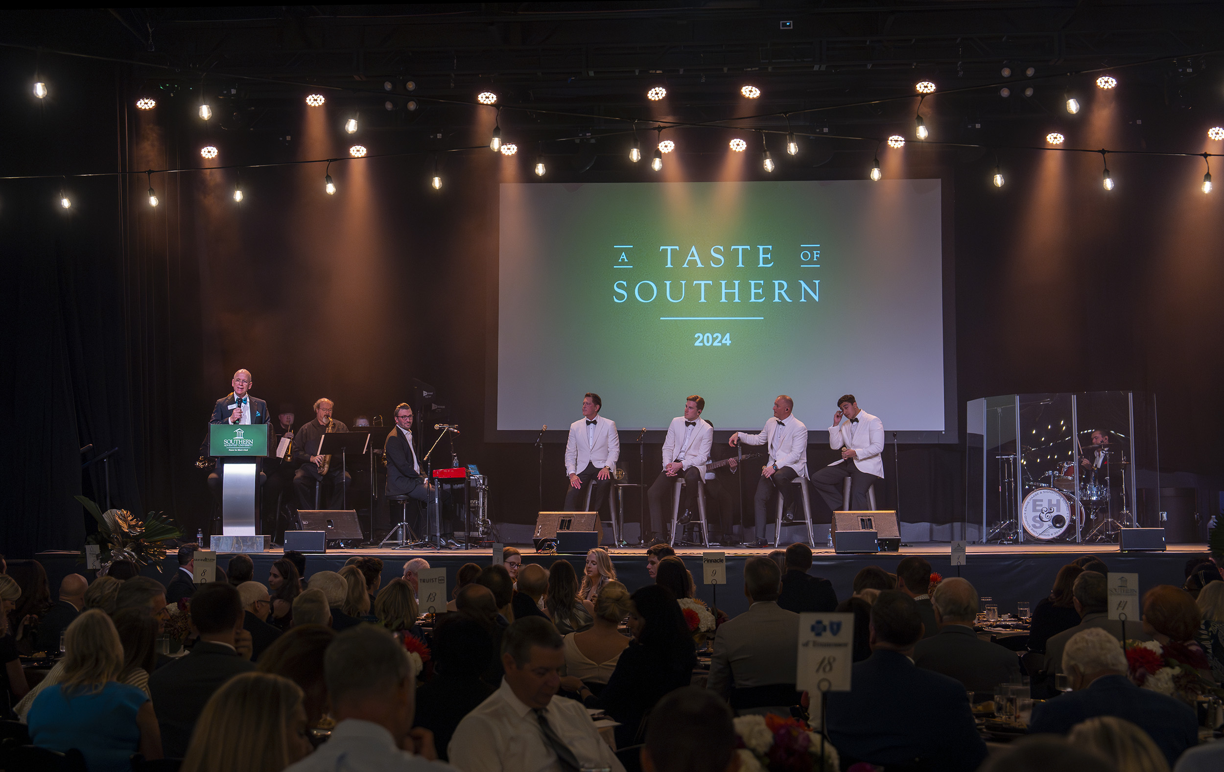 A view of the front stage with Ken Shaw, university president, speaking and musical guests Ernie Haase & Signature Sound looking on.