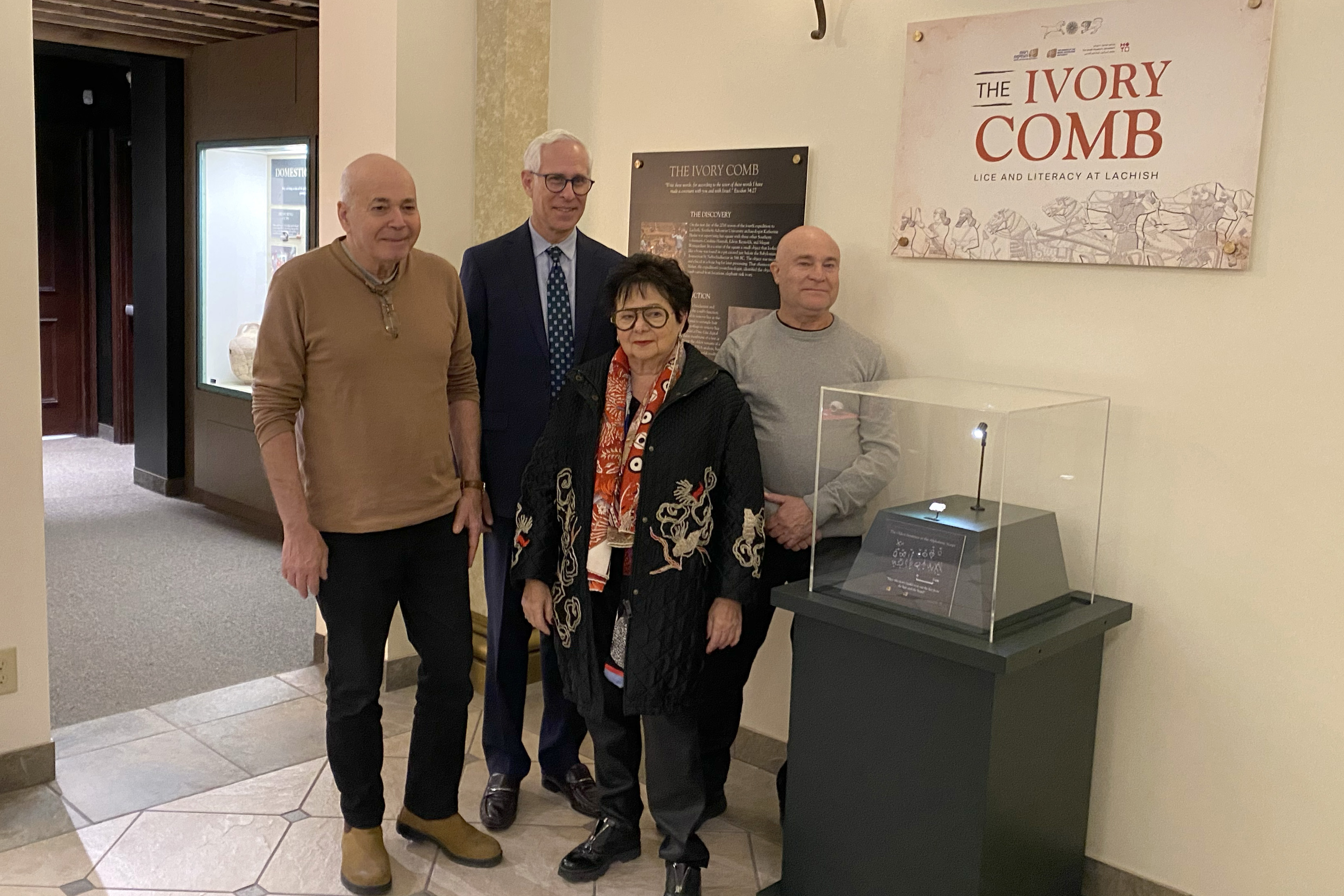 A group of prominent archaeologists stands next to the ivory comb exhibit at Southern Adventist University